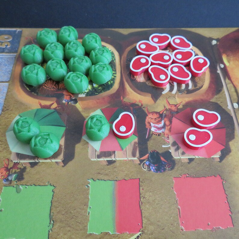 May include: A game board with green and red game pieces. The green pieces are shaped like cabbages and the red pieces are shaped like steaks. There are also two smaller game boards with green and red pieces.