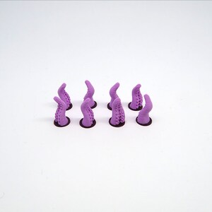May include: Eight purple plastic octopus tentacles, each with suction cups, are arranged in two rows of four on a white surface.