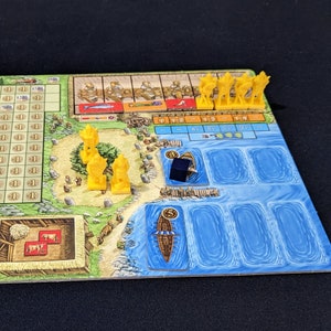 May include: A board game with a wooden board, yellow plastic pieces, and a blue and white water section. The board has a grid with numbers and letters. There are also small wooden pieces on the board. The game is called "The Voyages of Marco Polo".
