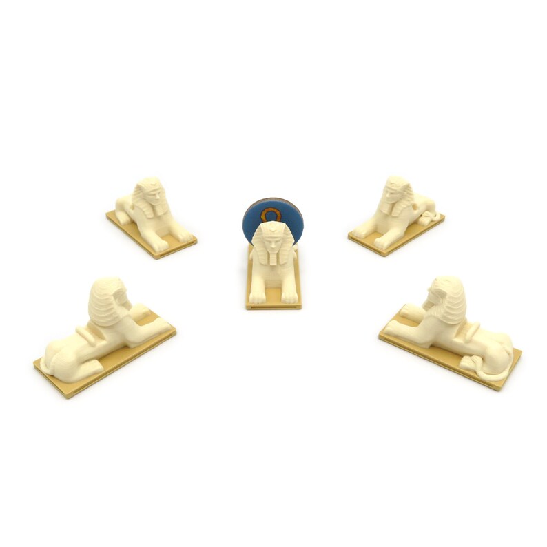 May include: Five white sphinx figurines, each with a gold trim, are arranged in a circle around a blue and gold circular object. The object has the number "8" on it.