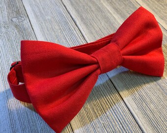 May include: A bright red bow tie made of fabric. The bow tie is tied and ready to wear.