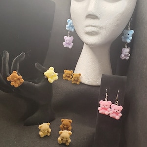 May include: Assortment of plush teddy bear earrings and rings in various colors, including pink, blue, yellow, and brown. The earrings are dangle style and the rings are adjustable.