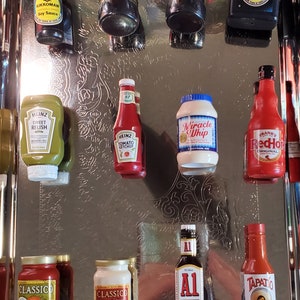 May include: A silver tray with ten miniature bottles of condiments, including soy sauce, ketchup, relish, mayonnaise, and hot sauce. The bottles are arranged in two rows, with the top row containing four bottles and the bottom row containing six bottles.