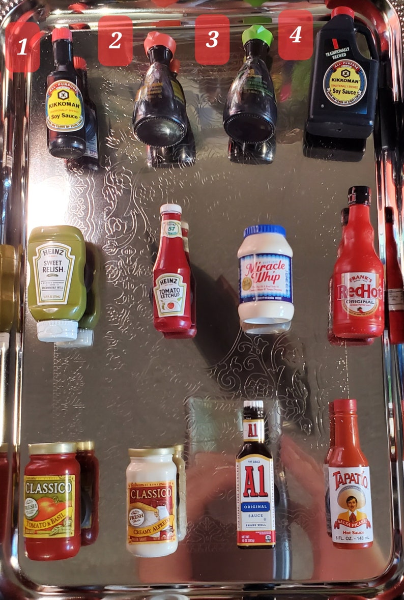 May include: A silver tray with ten miniature bottles of condiments, including soy sauce, ketchup, relish, mayonnaise, and hot sauce. The bottles are arranged in two rows, with the top row containing four bottles and the bottom row containing six bottles.