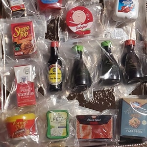 May include: A tray of miniature grocery items, including a box of Stove Top Chicken Stuffing, a bottle of soy sauce, a box of pure vanilla extract, a container of Hormel Chili, a container of feta cheese, a package of Black Label bacon, a box of flax seeds, and a package of Babybel cheese.