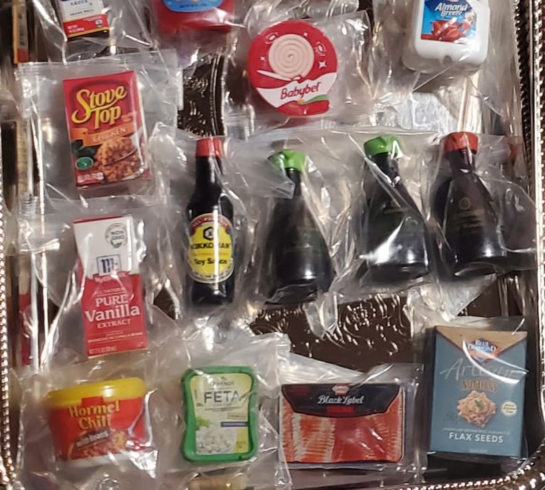 May include: A tray of miniature grocery items, including a box of Stove Top Chicken Stuffing, a bottle of soy sauce, a box of pure vanilla extract, a container of Hormel Chili, a container of feta cheese, a package of Black Label bacon, a box of flax seeds, and a package of Babybel cheese.
