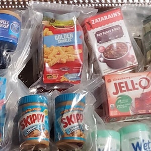 May include: A variety of miniature food and household items in clear plastic bags. The items include a box of Golden Crinkles, a box of Zatarains Red Beans & Rice, a jar of Skippy Creamy Peanut Butter, a box of Jell-O Strawberry Gelatin, a box of Pez candy, a jar of Maxwell House coffee, a can of Claussen pickles, and a bottle of Wet Ones wipes.