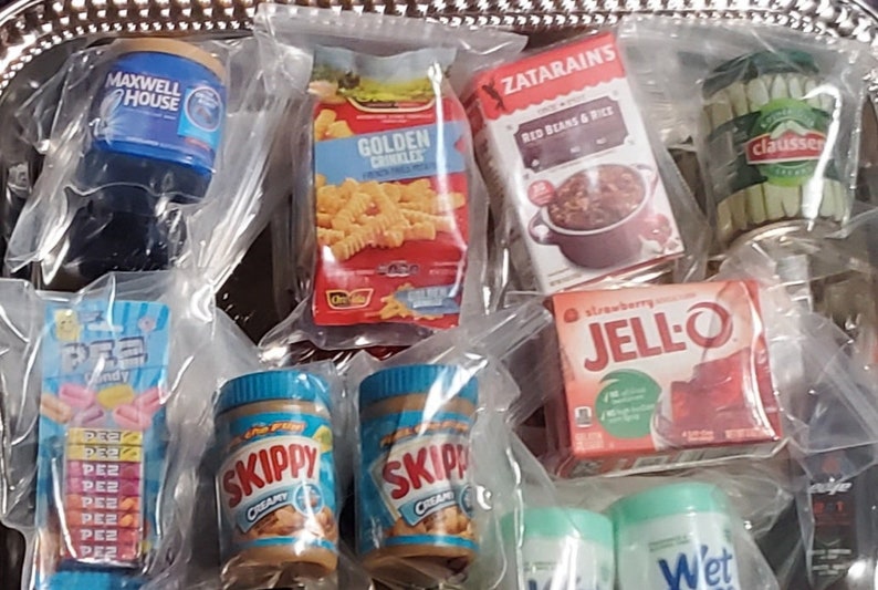 May include: A variety of miniature food and household items in clear plastic bags. The items include a box of Golden Crinkles, a box of Zatarains Red Beans & Rice, a jar of Skippy Creamy Peanut Butter, a box of Jell-O Strawberry Gelatin, a box of Pez candy, a jar of Maxwell House coffee, a can of Claussen pickles, and a bottle of Wet Ones wipes.