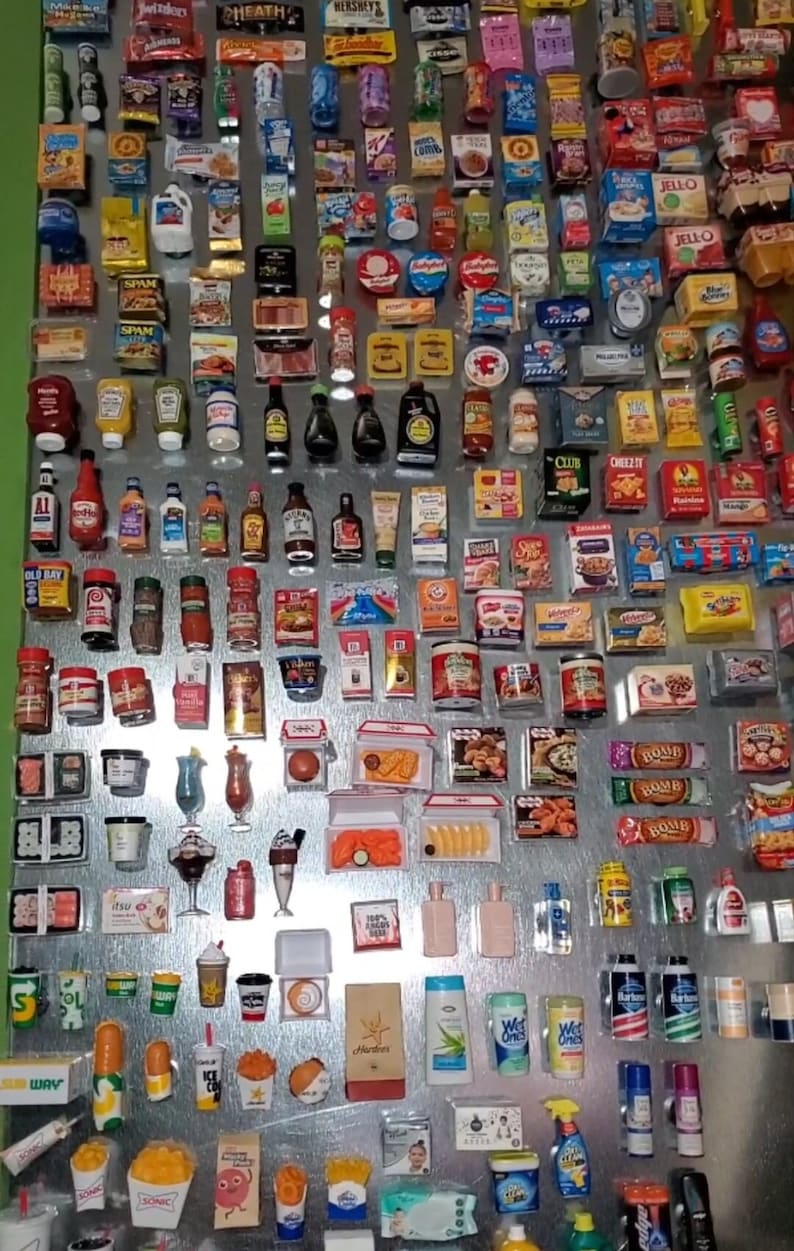 May include: A collection of miniature grocery items, including food, drinks, and household products, displayed on a silver metal surface. The items are arranged in rows and columns, creating a colorful and visually appealing display. Some of the items include: Spam, Jell-O, Cheez-It, Old Bay seasoning, and various brands of soda and juice.