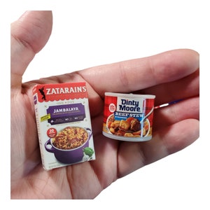 May include: A box of Zatarain's One-Pot Jambalaya mix and a can of Dinty Moore Beef Stew. The box is red and white with a picture of a pot of jambalaya. The can is red and white with a picture of beef stew.