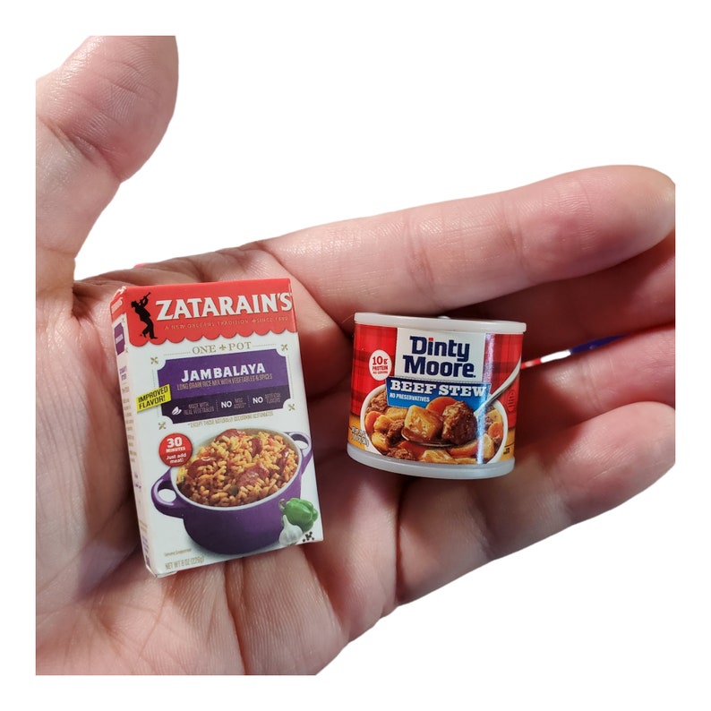 May include: A box of Zatarain's One-Pot Jambalaya mix and a can of Dinty Moore Beef Stew. The box is red and white with a picture of a pot of jambalaya. The can is red and white with a picture of beef stew.