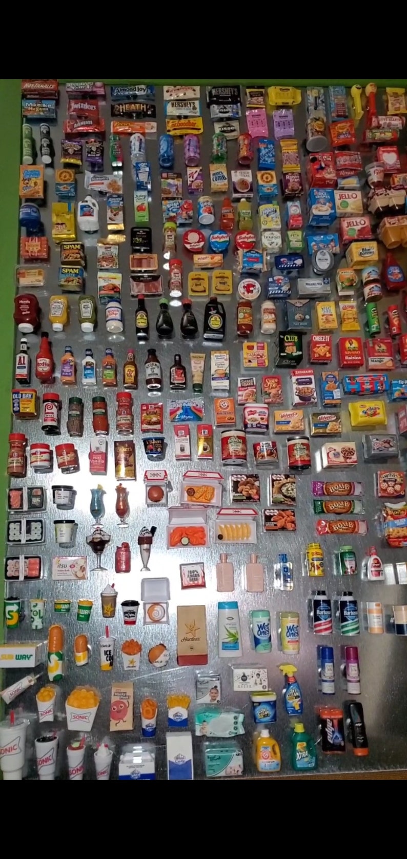 May include: A collection of miniature grocery and fast food items, including brands like Hershey's, Cheez-It, Jell-O, and Sonic. The items are arranged on a silver surface and include a variety of food items, drinks, and household products.