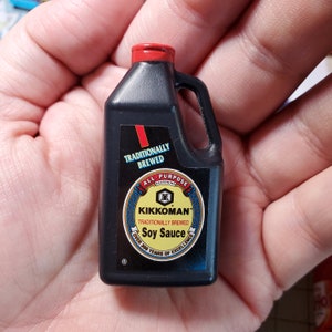 May include: A black plastic bottle of Kikkoman soy sauce. The bottle has a red cap and a white label with the text "TRADITIONALLY BREWED ALL-PURPOSE SEASONING KIKKOMAN TRADITIONALLY BREWED Soy Sauce OVER 300 YEARS OF EXCELLENCE".