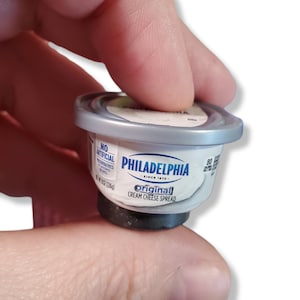 May include: A small, silver-colored plastic container of Philadelphia Original Cream Cheese Spread. The container is labeled "No Artificial Preservatives" and "Original Cream Cheese Spread".