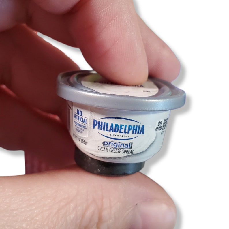 May include: A small, silver-colored plastic container of Philadelphia Original Cream Cheese Spread. The container is labeled "No Artificial Preservatives" and "Original Cream Cheese Spread".