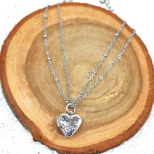 May include: A silver heart-shaped locket necklace with a delicate chain. The locket has a floral design and a small latch.