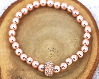 May include: A rose gold beaded bracelet with a rose gold charm accented with clear rhinestones.