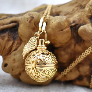 Puede incluir: Un collar de oro con una cadena delicada y un colgante redondo adornado. El colgante es un diseño de jaula con detalles florales y un pequeño amuleto de hoja adjunto. El colgante está abierto y parece ser un medallón.