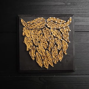 May include: A black wooden frame with a yellow string art design of a beard. The string art is made with nails and string.