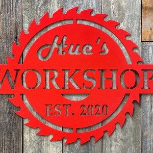 May include: Red metal sign shaped like a saw blade with the text "Hue's Workshop Est. 2020"