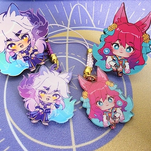 Puede incluir: Cuatro colgantes de estilo anime con personajes parecidos a zorros. Dos tienen pelaje blanco y morado, los otros dos rosa. Cada colgante tiene un cordón con un cierre dorado.