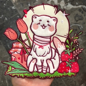 Könnte beinhalten: Ein bestickter Aufnäher mit einem weißen Frettchen mit rosa Wangen, zentriert vor einem cremefarbenen kreisförmigen Hintergrund. Das Design umfasst rote Tulpen, ein Glas mit kariertem Deckel, grünes Gras und rote Erdbeeren mit grünen Blättern.