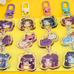 May include: Twelve colorful acrylic keychains featuring cartoon characters. Each keychain has a top charm with a character's face and a bottom charm with a smaller character. The characters are a mix of humans and animals, with some wearing hats and accessories.
