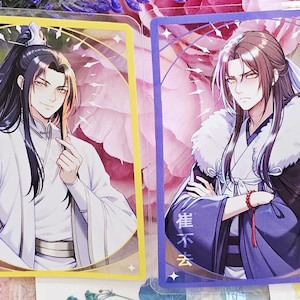 Peut inclure: Deux cartes de personnages de style anime. L'une représente un homme en robe blanche avec de longs cheveux noirs, l'autre un homme en robe bleue et noire avec un col en fourrure. Les deux cartes ont une bordure décorative et sont sur un fond floral.