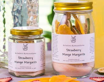 May include: Two glass jars and two glass bottles containing Strawberry Mango Margarita mix. The jars have gold lids and white labels with the text Kristin's Koncoctions Strawberry Mango Margarita. Dried fruit slices are scattered on the surface.