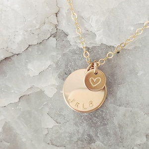 Peut inclure: Collier en or avec deux pendentifs. Le plus grand pendentif est un disque rond avec les initiales "JKLB" gravées dessus. Le plus petit pendentif est un cœur avec un petit cœur gravé à l'intérieur.