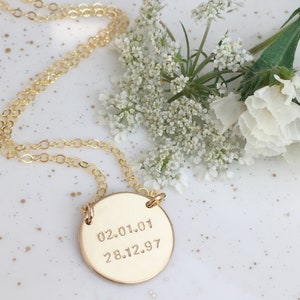 Peut inclure: Un collier en chaîne dorée avec un pendentif rond gravé des dates "02.01.01" et "28.12.97".