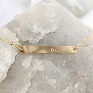 May include: Gold bar necklace with a delicate chain and the initials "D.J.V.C." engraved on the bar.