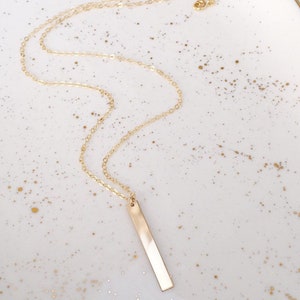 May include: A gold chain necklace with a long, thin, rectangular pendant.