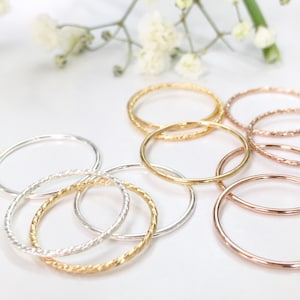 May include: A set of thin, twisted metal rings in gold, silver, and rose gold. The rings are stacked and overlapping.