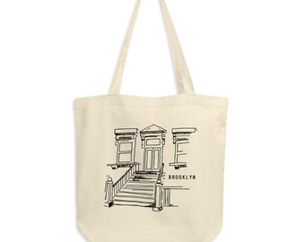 May include: A beige tote bag featuring a black line drawing of a Brooklyn brownstone with a door and steps. The text "BROOKLYN" is printed below the drawing.