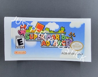 May include: A sticker for a Game Boy Advance game cartridge featuring the Super Mario Advance logo with a blue sky, green grass, and a red-and-white mushroom. The sticker also includes the ESRB rating of "Everyone" and the Nintendo Seal of Quality.