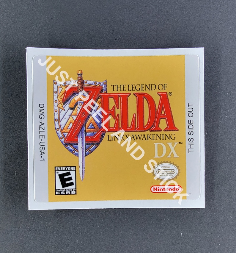May include: A yellow and red game cartridge label for the game "The Legend of Zelda: Link's Awakening DX" for the Game Boy Color. The label features a sword and shield with the game title and logo. The label also includes the ESRB rating "Everyone" and the Nintendo seal of quality.