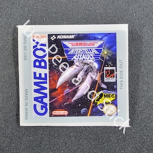 Puede incluir: Un cartucho de Game Boy para el juego "Gradius: Interstellar Assault" de Konami. El cartucho es azul y blanco con una imagen de una nave espacial en el espacio. El texto "Official Game Boy Game Pak" está impreso en el cartucho.