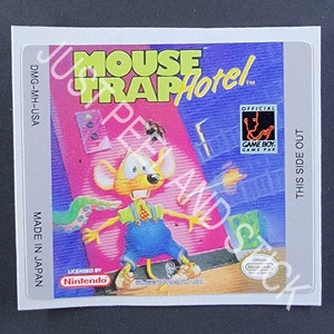May include: A Game Boy game cartridge for Mouse Trap Hotel. The cartridge is white with a silver label. The label features a cartoon mouse in a blue jumpsuit and a pink and blue background. The text on the label reads "Mouse Trap Hotel" and "Official Game Boy Game Pak".