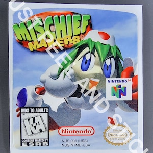 Puede incluir: Un cartucho de juego de Nintendo 64 para Mischief Makers. El juego está clasificado como "K-A" por la ESRB. El cartucho es blanco con un personaje rojo, verde y azul en la parte delantera. El texto "Nintendo 64" y el logotipo de Nintendo 64 son visibles en el cartucho.