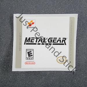 May include: A white Game Boy Color game cartridge label for Metal Gear Solid. The label features the game's title, a Konami logo, an ESRB rating of "Everyone", and a Nintendo licensed logo.