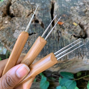 May include: Three bamboo crochet hooks with metal tips. The hooks are held in a hand.