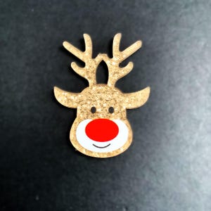 May include: Gold glitter reindeer head ornament with a red nose and white face.