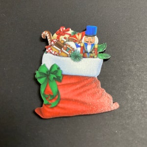 May include: A wooden Christmas stocking decoration filled with gifts, candy canes, and a toy soldier. The stocking is red with a green bow, and the top is white. A festive holiday decoration.
