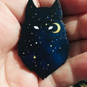 Pu&ograve; includere: Una silhouette di lupo in legno con una luna crescente e stelle su uno sfondo blu scuro.