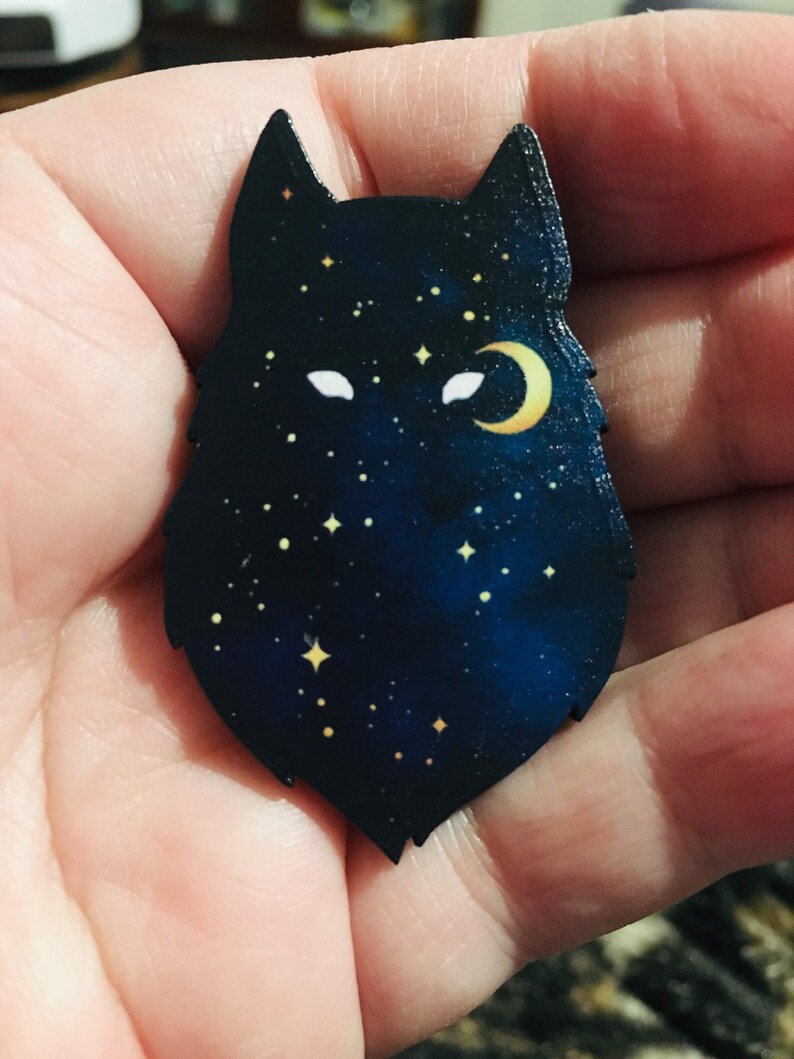 Pu&ograve; includere: Una silhouette di lupo in legno con una luna crescente e stelle su uno sfondo blu scuro.