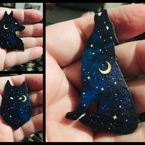 Pu&ograve; includere: Una silhouette di lupo in legno nero con una luna crescente e stelle dipinte su di essa. Il lupo sta ululando alla luna.