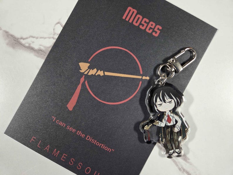 May include: A keychain featuring an anime-style character with black hair, a white shirt, and a red tie. The keychain is attached to a black card with the name "Moses" and the text "I can see the Distortion" in red.