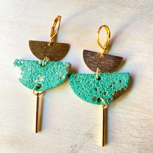 May include: A pair of handcrafted earrings with a unique design. Each earring features a half-circle of dark brown metal, a turquoise suede-like half-circle with gold accents, and a gold bar pendant. The earrings have gold-colored lever-back closures.