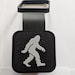 A black and white tail hitch cover made of rubber with a 3d printed image of a Sasquatch